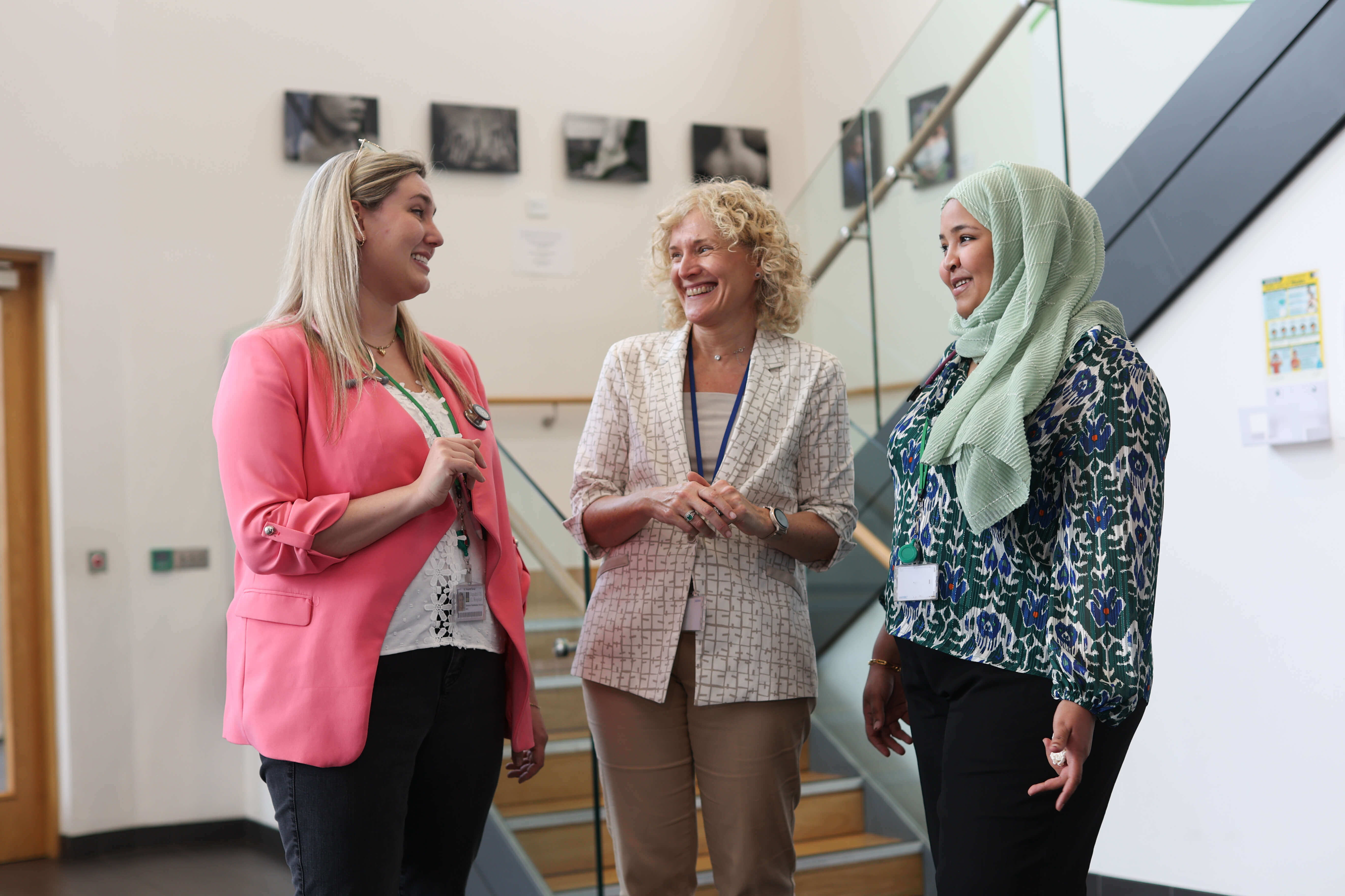 Three smiling female doctors have a conversation in a hospital corridor